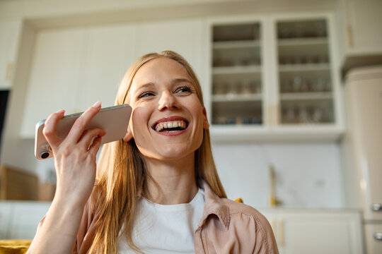 Smiling young woman using voice assistant in home kitchen