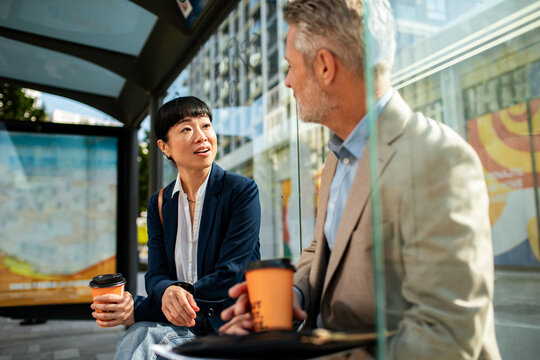 Business colleagues talking with coffee at city bus stop