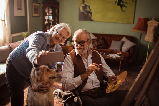 Senior couple taking selfie with dog while painting at home
