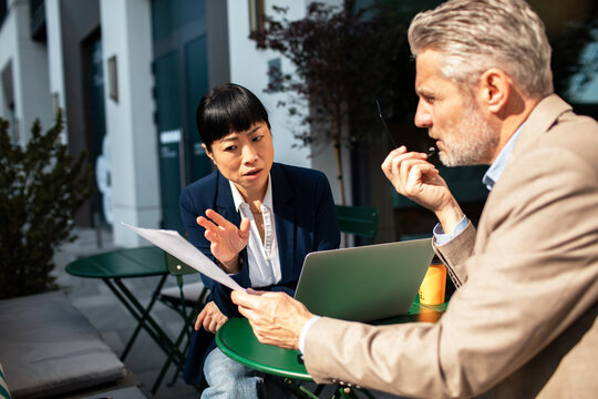 Two business professionals reviewing documents at outdoor cafe