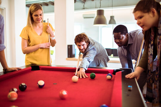 Coworkers playing pool during break in modern office