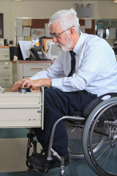 Man with Muscular Dystrophy in a wheelchair filing papers in his office drawer