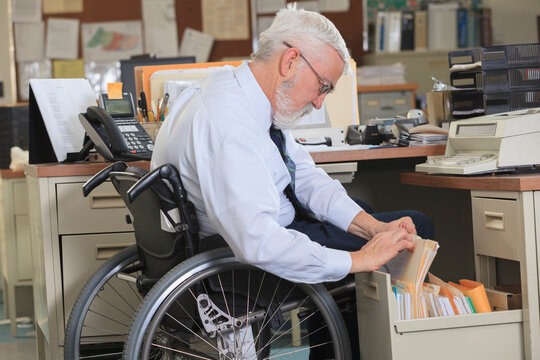 Man with Muscular Dystrophy in a wheelchair looking up paperwork in his office drawer