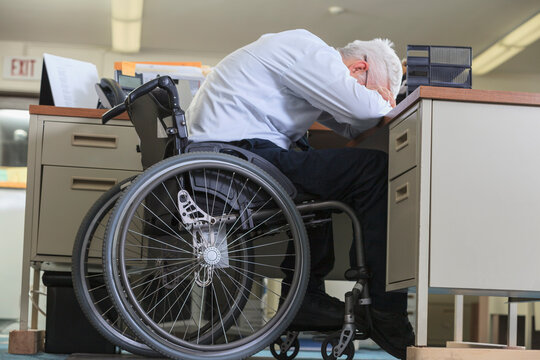 Man with Muscular Dystrophy in a wheelchair leaning down on his office desk