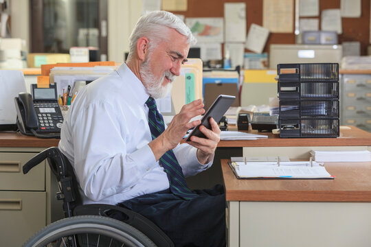 Man with Muscular Dystrophy in a wheelchair using a tablet at his office desk