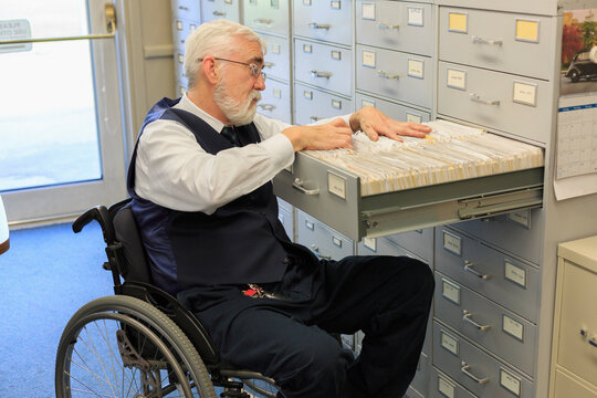 Man with Muscular Dystrophy in a wheelchair using a filing system in his office