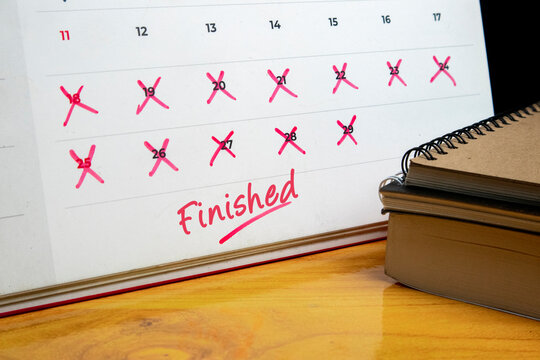 Desk calendar with crossed out dates and handwritten red finished text next to spiral notebooks