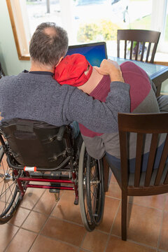 Young man with Down Syndrome hugging his father in wheelchair with Spinal Cord Injury at home