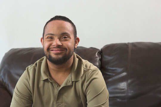 Portrait of happy African American man with Down Syndrome sitting on couch at home