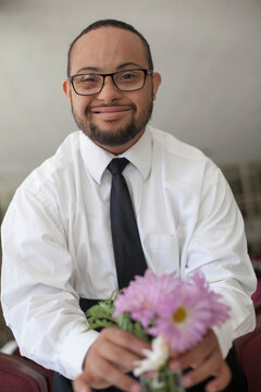 Portrait of happy African American man with Down Syndrome as a waiter fixing flowers in vase on