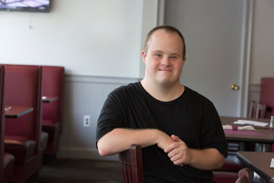 Portrait of happy waiter with Down Syndrome sitting on chair in a restaurant