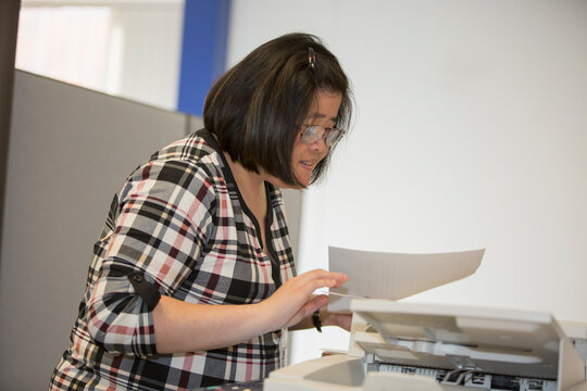 Asian woman with a Learning Disability working at a copy machine in office