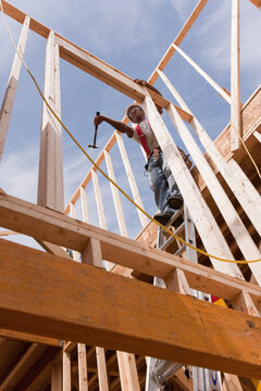Carpenter using a hammer on the wall frame on the second floor of a house under construction