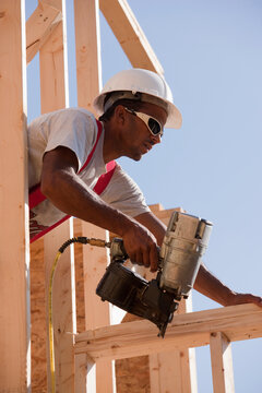 Hispanic carpenter using a nail gun on a window frame