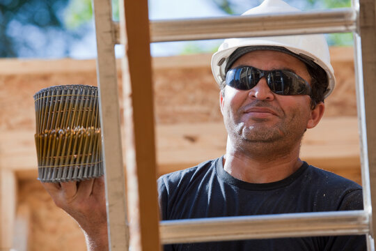 Hispanic carpenter holding two coils of nails on a ladder at a house under construction