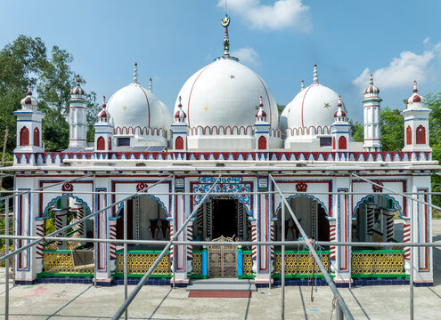Aerial view of a white mosque with three large domes and colorful architectural details surrounded by greenery in Joypurhat, Rajshahi Division, Bangladesh.