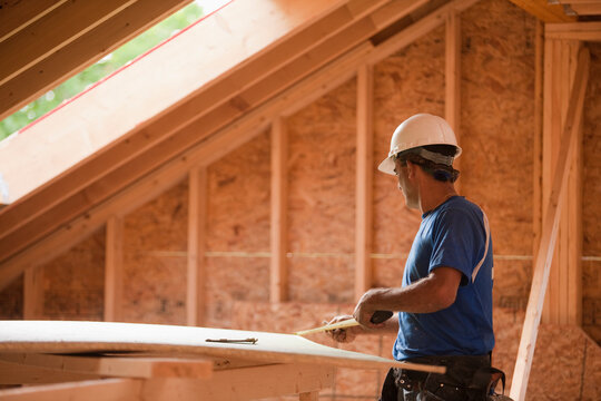 Hispanic carpenter measuring a piece of sheathing at a house under construction