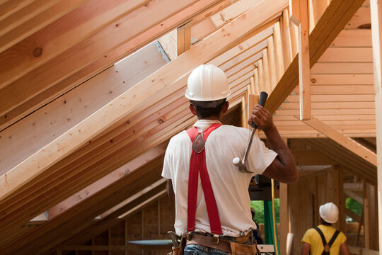 Hispanic carpenter using hammer on upper floor at a house under construction
