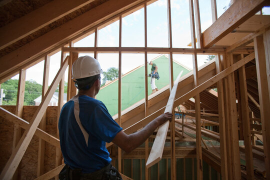 Hispanic carpenters bringing construction trim strip up to roof of a house under construction