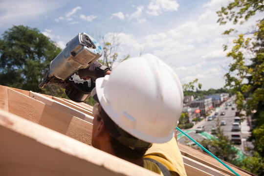 Hispanic carpenter using a nail gun at a house under construction