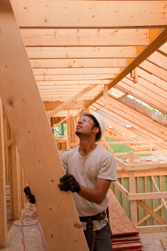 Hispanic carpenter passing up a rafter to roof at a house under construction
