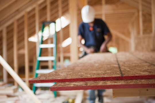 Carpenter using a circular saw on particle board in a house under construction