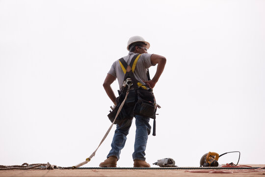 Hispanic carpenter standing on the roofing with a hammer, circular saw and a nail gun