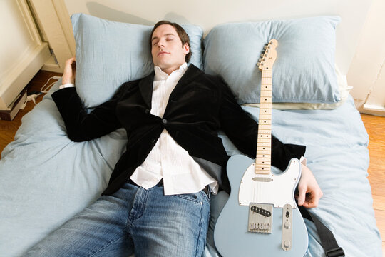 Man sleeping in bed with guitar