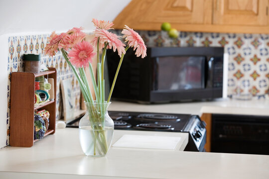 A flower vase with pink daisies in a kitchen