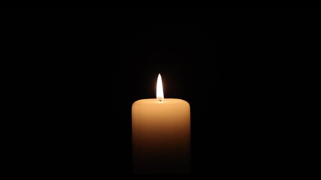 Close-up video of a burning white candle with a steady flame against a deep black background. Minimalistic scene symbolizing remembrance, hope, spirituality, meditation, mourning, peace, faith and ref
