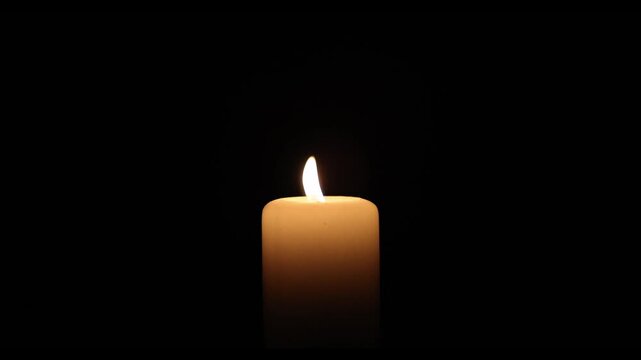 Close-up video of a burning white candle with a steady flame against a deep black background. Minimalistic scene symbolizing remembrance, hope, spirituality, meditation, mourning, peace, faith and ref