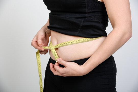 Frau misst ihren Bauchumfang mit einem Ma&szlig;band. Symbolbild f&uuml;r Abnehmen, Gewichtsreduktion, Fitness, Di&auml;t, K&ouml;rperbewusstsein, gesunde Ern&auml;hrung und pers&ouml;nliche Gesundheitsziele. Echtfoto.