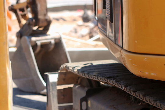 Close-up view of heavy construction equipment tracks and bucket at a dusty urban job site, focusing on industrial machinery details and rugged work environment.