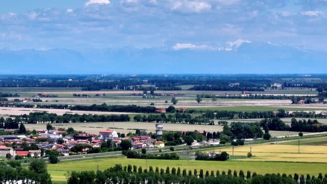 High angle drone view over small countryside villages and green agricultural fields of the Venetian plain, looking towards the distant Alps mountain range in daylight, Eraclea, Italy
