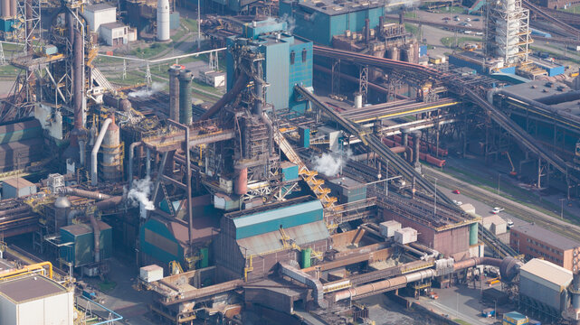 Aerial view of the Tata Steel industrial complex featuring blast furnaces, intricate pipe networks, and conveyor belts under soft daylight in Velsen-Noord, Noord-Holland, Netherlands.
