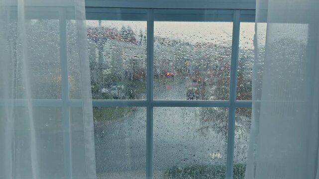 Gentle raindrops trace patterns on the window, creating a serene atmosphere inside a warm room. Outside, the vibrant world remains alive with life despite the rain