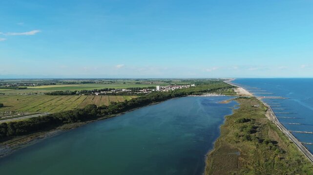 High angle wide drone perspective of the narrow sandy peninsula separating the Venetian Lagoon wetlands from the open Adriatic Sea at sunset near Eraclea and the Piave mouth, Italy