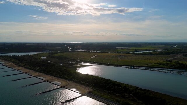 drone overflight showcasing strong sunset backlight reflecting over wet mudflats, sandy shores and narrow channels of the Venetian Lagoon near Eraclea, Italy