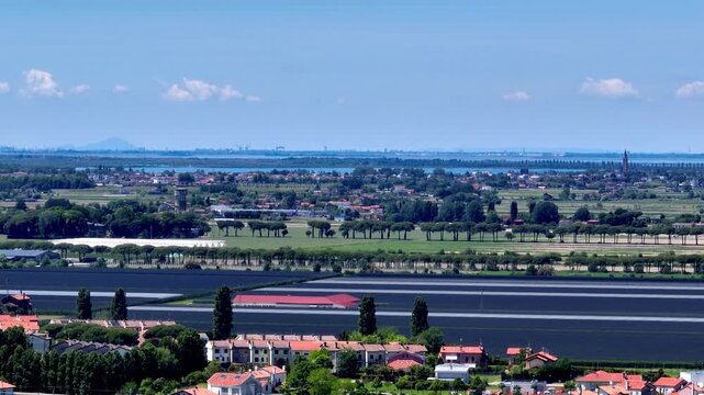 aerial drone tracking shot over green rural vineyards on the Venetian plain, looking towards the massive industrial hub of Porto Marghera on the hazy horizon, Italy