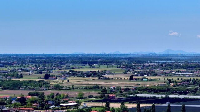 Distant wide drone panorama looking over the green Venetian plain countryside towards the massive industrial factories and smoking chimneys of Porto Marghera hub in daylight, Italy
