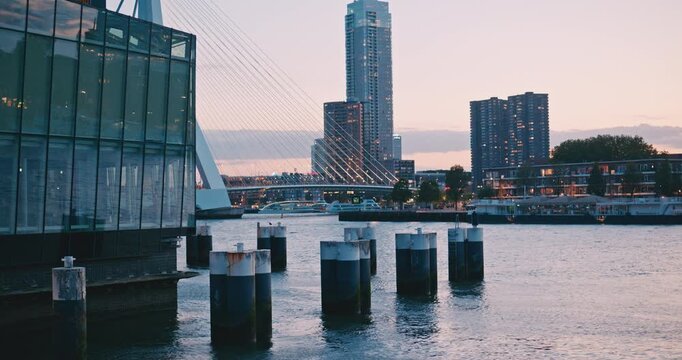Contemporary waterfront cityscape with mooring posts in the river, cable-stayed bridge and modern skyscrapers skyline at twilight evening dusk.