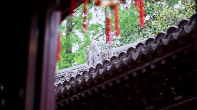 Stone figures adorn the roofline of a traditional Chinese building, framed by red lanterns. Ideal for cultural documentaries or architectural studies.