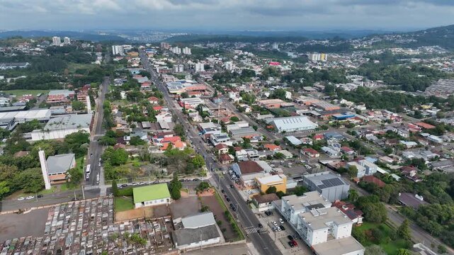 Ivoti main road seen from above with an orbit counterclockwise camera movement, showing residential and commercial buildings, distant hills, and cloudy sky.