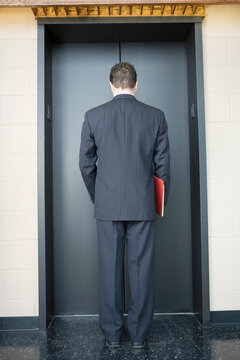 Rear view of a businessman waiting for the elevator in an office building