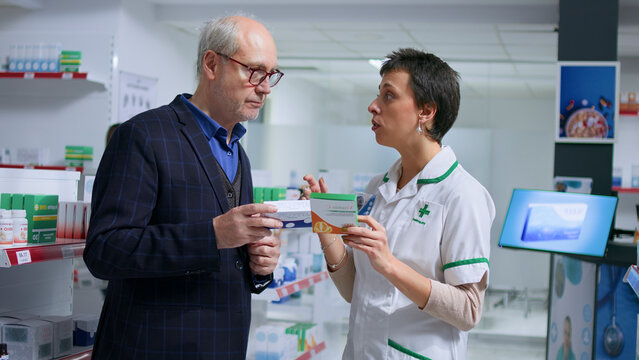 Elderly man feeling unwell visiting chemist shop, looking to find pharmaceutical product to cure nauseating ailment, asking trained healthcare expert for product suggestions