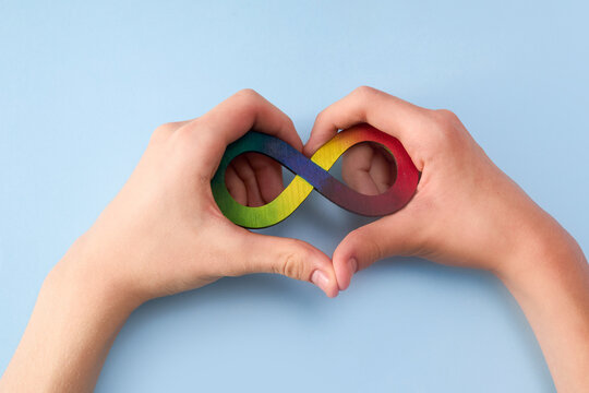 Hands making heart shape with rainbow infinity symbol on blue background. Neurodiversity and autism acceptance day concept.