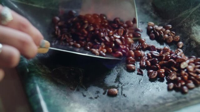 Close-up of a barista's hand roasting coffee beans with fire and herbal liqueur on a green stone surface. Artisanal flambe process using steel spatulas inside a boutique cafe