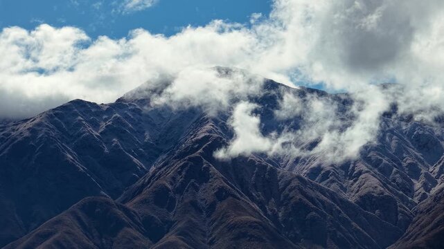 Low clouds passing through snow capped rocky heights in the Andes mountain range.