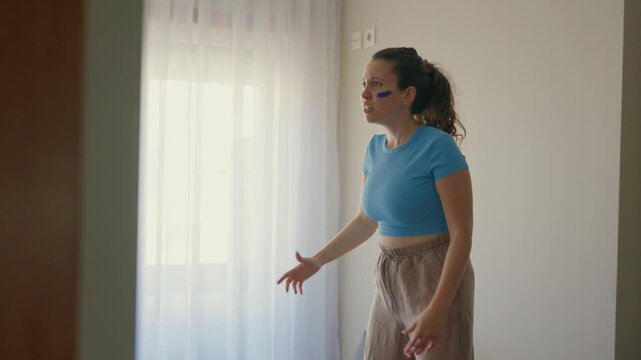 Anxious and passionate sports fan standing on sofa reacting angrily to TV match. Female supporter in blue clothes angry mad with result of game play screams in disappointment at screen in apartment