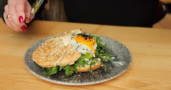 Diner spears arugula with fork and lifts fresh leafy forkful toward mouth. Knife steadies bun and yolk glistens on plate while person prepares next bite